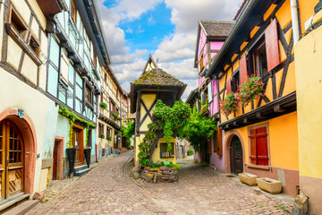 A picturesque alley with two paths surrounded by colorful half-timbered medieval homes in the French village of Eguisheim, France, in the Alsace region.