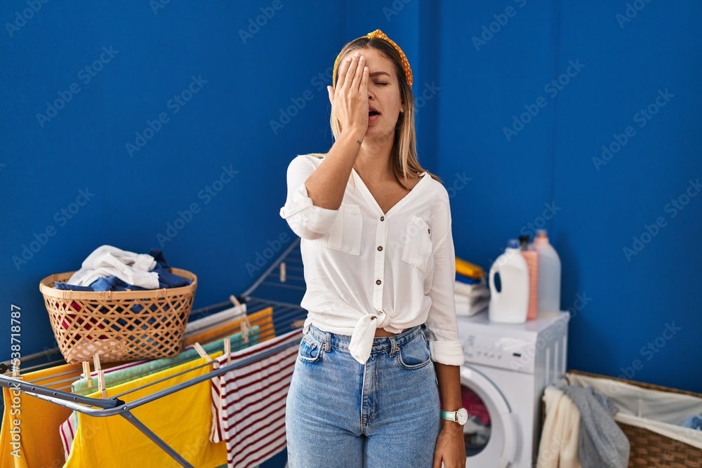 Sticker Young blonde woman at laundry room yawning tired covering half face, eye and mouth with hand. face hurts in pain.