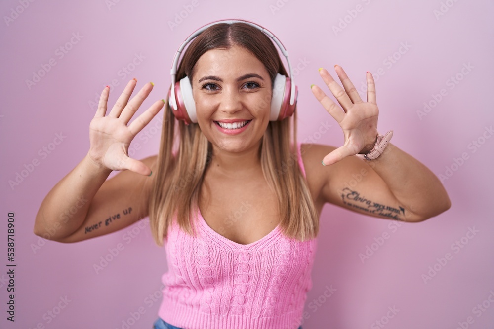 Sticker Young blonde woman listening to music using headphones showing and pointing up with fingers number ten while smiling confident and happy.