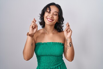 Fototapeta na wymiar Young hispanic woman standing over isolated background gesturing finger crossed smiling with hope and eyes closed. luck and superstitious concept.