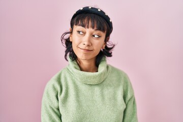 Young beautiful woman standing over pink background smiling looking to the side and staring away thinking.