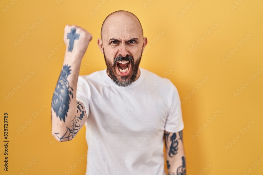 Canvas Prints young hispanic man with tattoos standing over yellow background angry and mad raising fist frustrate