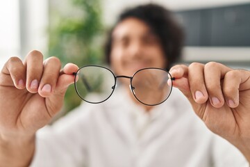 Young hispanic man optician holding glasses at clinic