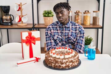 African man with dreadlocks celebrating birthday holding big chocolate cake skeptic and nervous, disapproving expression on face with crossed arms. negative person.
