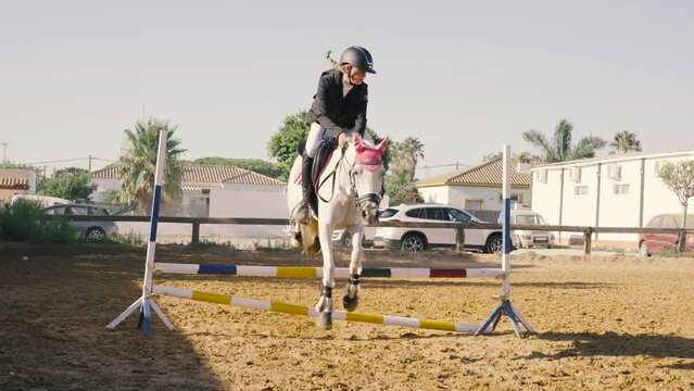 4K video of a 15 year old teenage girl jumping over obstacles on a white horse