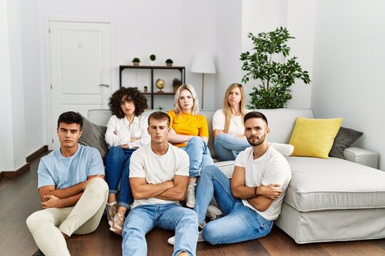 Group of people sitting on the sofa and floor at home skeptic and nervous, disapproving expression on face with crossed arms. negative person.