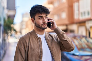 Young hispanic man talking on the smartphone at street