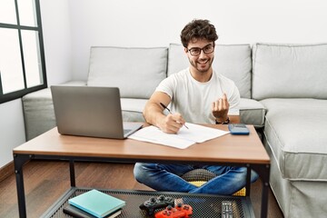 Fototapeta premium Hispanic man doing papers at home beckoning come here gesture with hand inviting welcoming happy and smiling