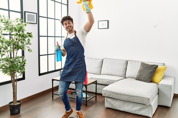 Young hispanic man dancing and holding cleaning sprayer and cloth at home