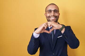 Hispanic man with beard wearing suit and tie smiling in love doing heart symbol shape with hands. romantic concept.