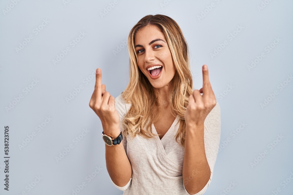 Poster young blonde woman standing over isolated background showing middle finger doing fuck you bad expres