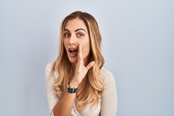 Young blonde woman standing over isolated background hand on mouth telling secret rumor, whispering...