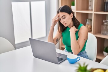 Young hispanic woman using laptop with worried expression at home