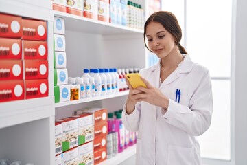 Young woman pharmacist using smartphone working at pharmacy