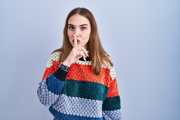 Young hispanic girl standing over blue background asking to be quiet with finger on lips. silence and secret concept.