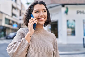 Young woman smiling confident talking on the smartphone at street