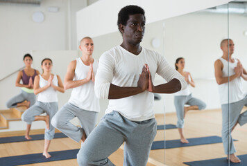 Young man maintaining healthy lifestyle practicing yoga asana at group class