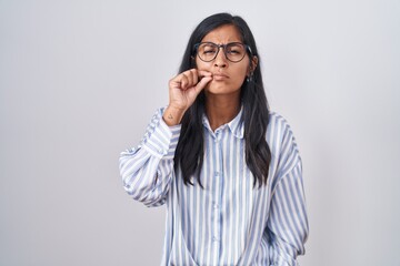 Young hispanic woman wearing glasses mouth and lips shut as zip with fingers. secret and silent, taboo talking