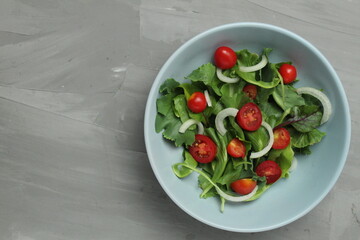 arugula salad of cherry tomato iceberg and sweet onions with a dressing in a setlo blue plate on a gray background with space for text. Healthy delicious food vegetables vitamins