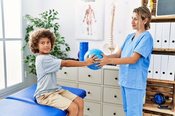 Mother and son wearing physiotherapist uniform having rehab session using ball at physiotherapy...