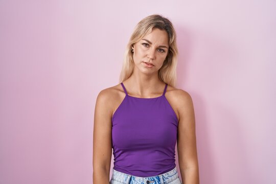 Young blonde woman standing over pink background looking sleepy and tired, exhausted for fatigue and hangover, lazy eyes in the morning.