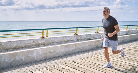 Middle age hispanic man wearing sportswear running at seaside