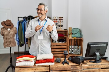 Middle age hispanic man working as manager at retail boutique pointing to the back behind with hand and thumbs up, smiling confident