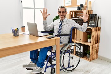 Middle age hispanic man working at the office sitting on wheelchair showing and pointing up with fingers number eight while smiling confident and happy.