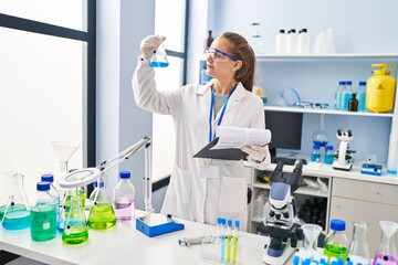 Fototapeta premium Young blonde woman wearing scientist uniform holding test tube and clipboard at laboratory