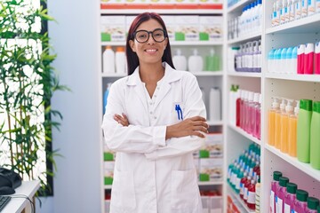 Young beautiful hispanic woman pharmacist smiling confident standing with arms crossed gesture at pharmacy