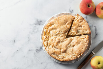 Apple pie Charlotte with apples and rustic knife on white marble background. Top view, flat lay...