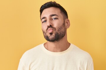 Fototapeta premium Handsome hispanic man standing over yellow background looking at the camera blowing a kiss on air being lovely and sexy. love expression.
