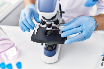Young hispanic man wearing scientist gloves using microscope at laboratory