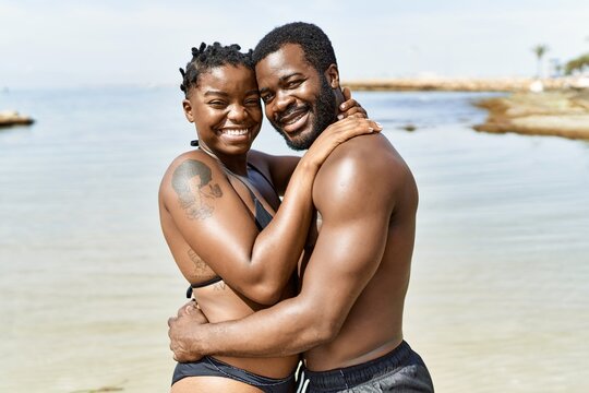 Young african american tourist couple wearing swimwear hugging at the beach.