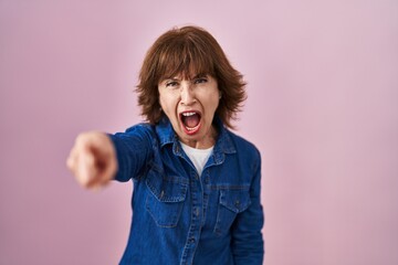 Middle age woman standing over pink background pointing displeased and frustrated to the camera, angry and furious with you