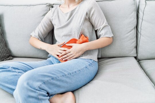 Young caucasian woman using hot water bag for period pain at home