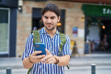 Young hispanic man tourist wearing backpack using smartphone at street