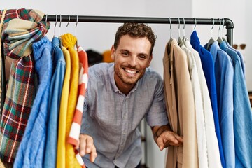 Young hispanic customer man smiling happy appearing through clothes at clothing store.