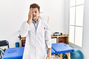 Obraz premium Handsome young man working at pain recovery clinic covering one eye with hand, confident smile on face and surprise emotion.