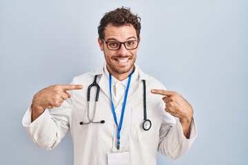 Fototapeta premium Young hispanic man wearing doctor uniform and stethoscope looking confident with smile on face, pointing oneself with fingers proud and happy.