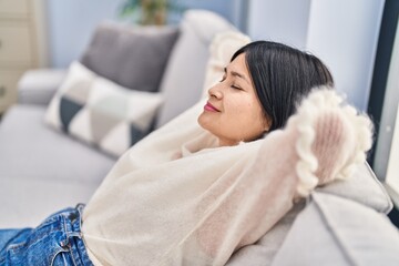 Young chinese woman relaxed with hands on head sitting on sofa at home