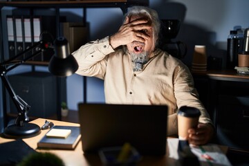 Obraz na płótnie Canvas Middle age man with grey hair working at the office at night peeking in shock covering face and eyes with hand, looking through fingers with embarrassed expression.
