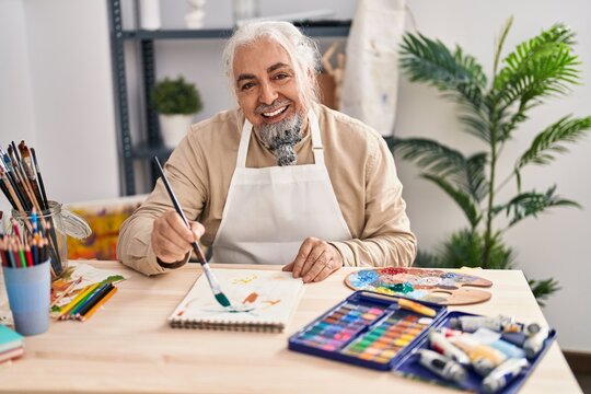 Middle age grey-haired man artist smiling confident drawing on notebook at art studio