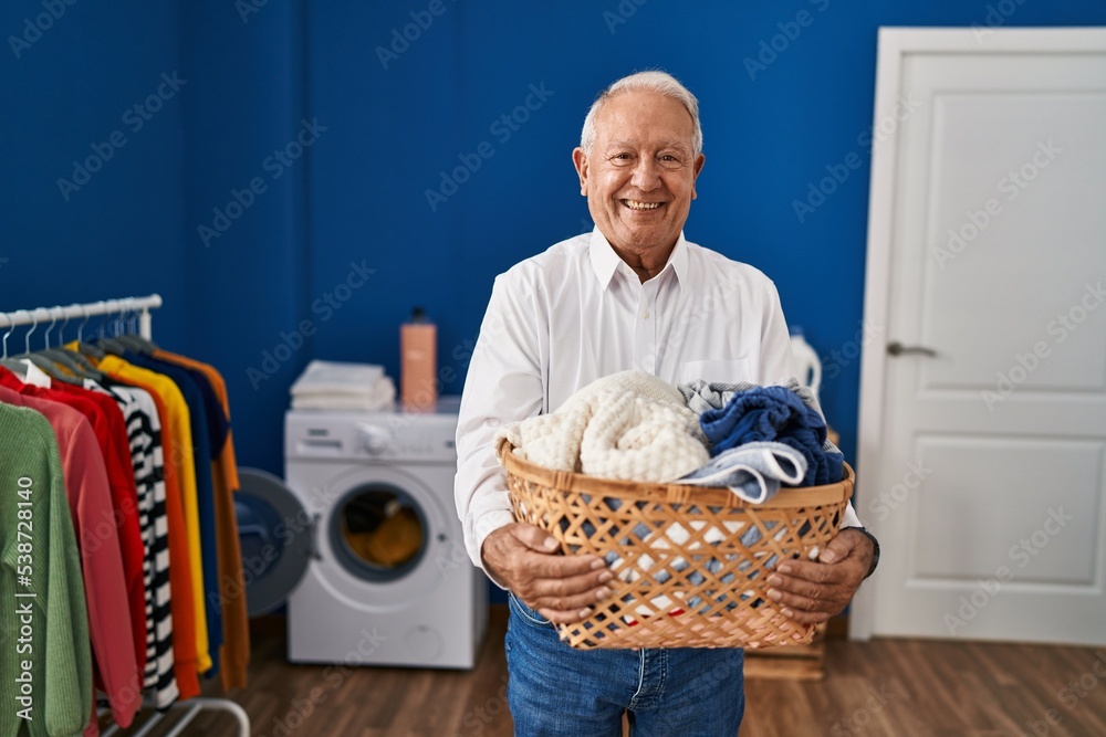 Sticker Senior man with grey hair holding laundry basket at home smiling with a happy and cool smile on face. showing teeth.