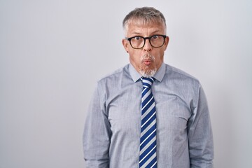 Hispanic business man with grey hair wearing glasses making fish face with lips, crazy and comical gesture. funny expression.