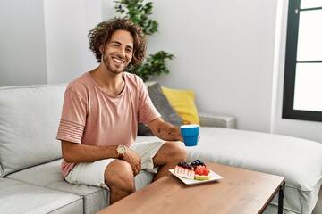 Fototapeta na wymiar Young hispanic man having breakfast sitting on the sofa at home.