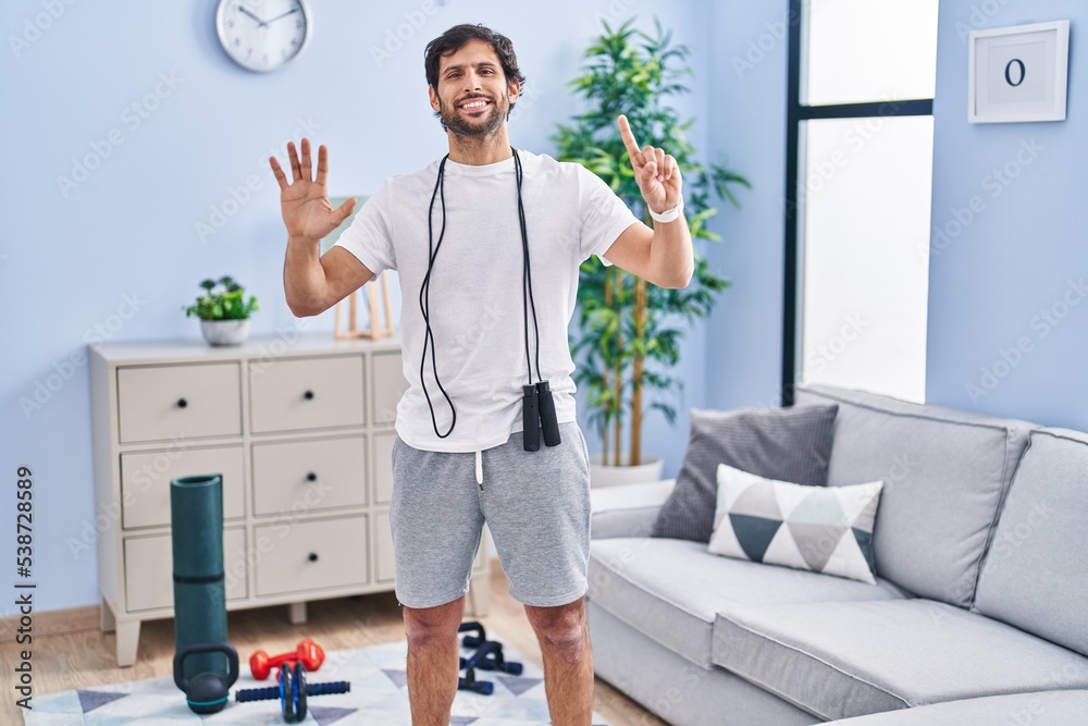 Poster handsome latin man wearing sportswear at home showing and pointing up with fingers number six while 