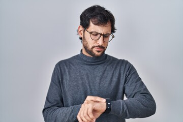 Handsome latin man standing over isolated background checking the time on wrist watch, relaxed and confident
