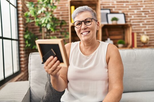 Middle age woman holding photo sitting on sofa at home