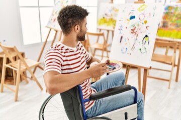 Young arab disabled artist man drawing sitting on wheelchair at art studio.